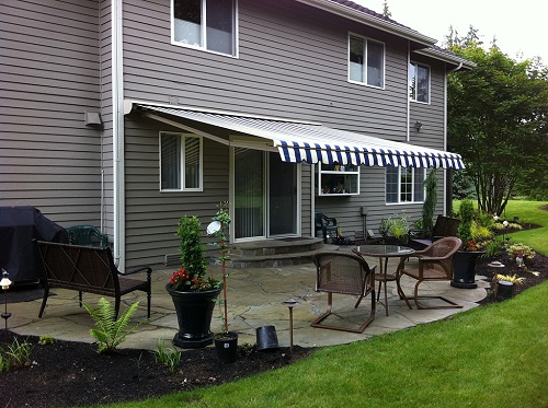 A gray house with a ray and white awning extended over a patio.