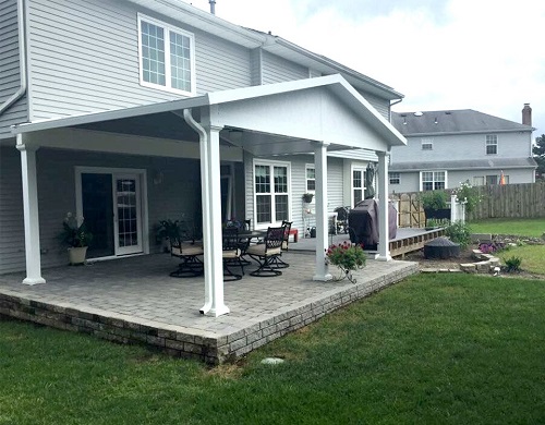 An outdoor patio with a solid-roofed cover overlooking a grass-covered yard.