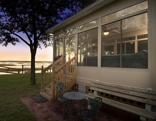 A white sunroom overlooking a lake at dusk.