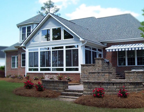 A gable-roofed sunroom extending from a red-bricked home with gray roofing shingles.
