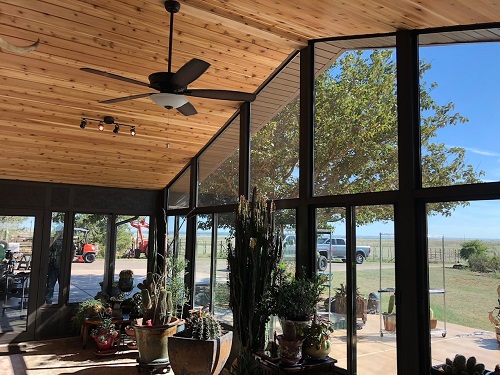 A large sunroom with vaulted wood ceilings overlooking a dirt road and grassy plain. 