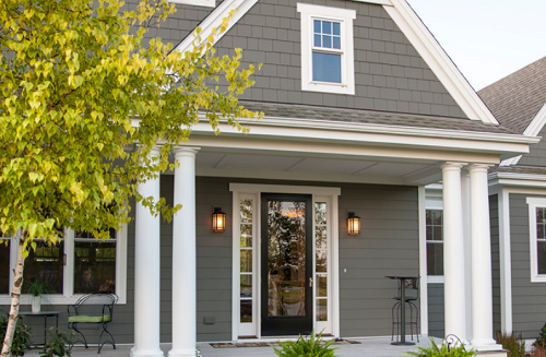 A house with gray siding and covered entryway with white pillars. 