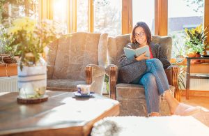 A woman smiling as she reads a book in a chair in her sunroom